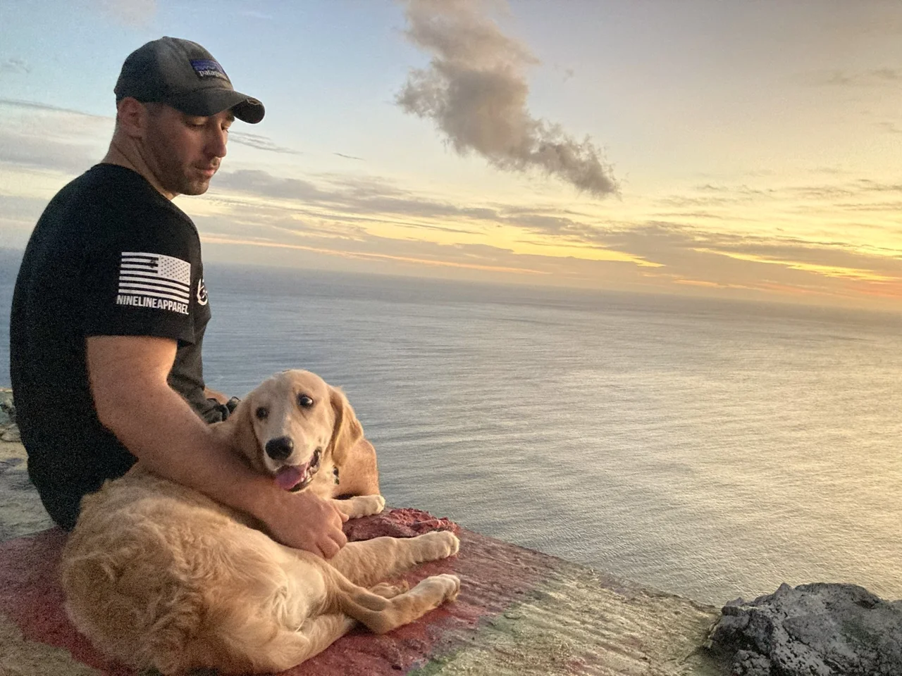 Ryan Adams with his golden retriever overlooking the ocean at sunset